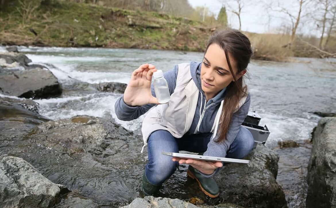photo of woman researcher taking water sample from creek